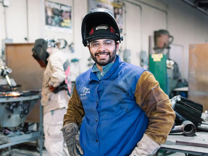 A student stands smiling in a welding class